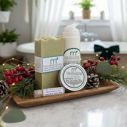 Muscle Relief Winter Wellness Set with natural soap, healing salve, lip balm, and lotion displayed in a holiday botanical spa scene